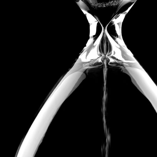 Sand flowing through an hourglass on black background concept for time running out